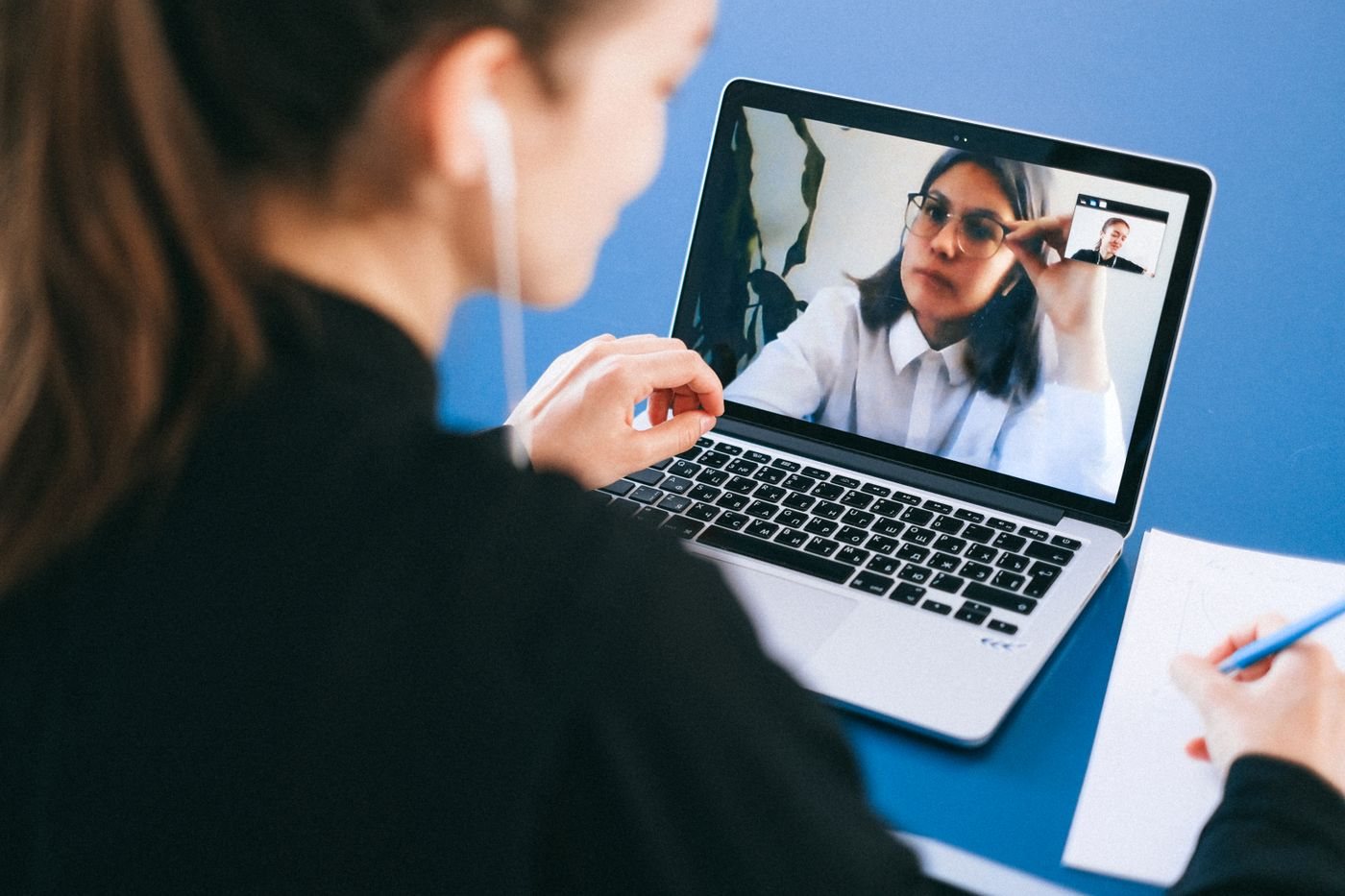 Person taking notes during a laptop video meeting